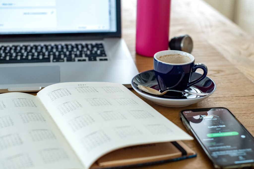 planner, phone, water and coffee in front of laptop